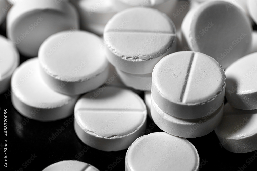 Close up of white painkiller tablet on a reflective black background Close up of white painkiller tablet on a reflective black background