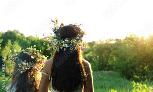 Fotografija Two girls in flower wreaths on meadow, sunny green natural background