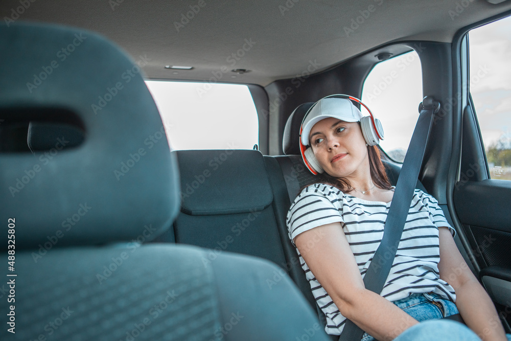 woman sitting at car rear sits listening music with headset
