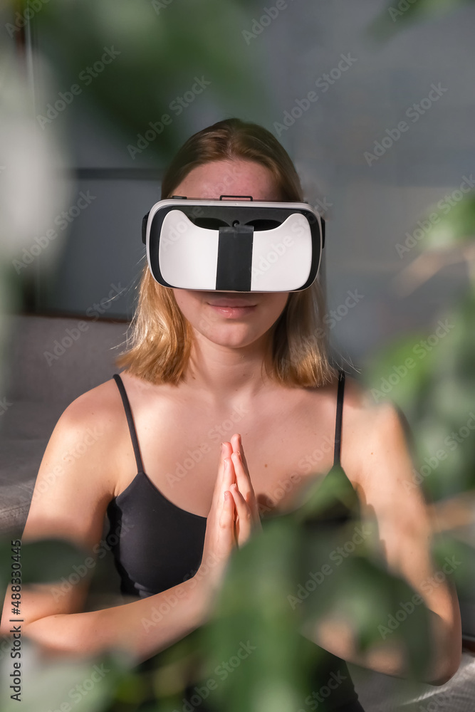 Nice girl using AR while meditating sitting in lotus position on roll mat wearing sports wear indoors,wellness, mental health, immersive reality,VR reality Nice girl using AR while meditating sitting in lotus position on roll mat wearing sports wear indoors,wellness, mental health, immersive reality,VR reality