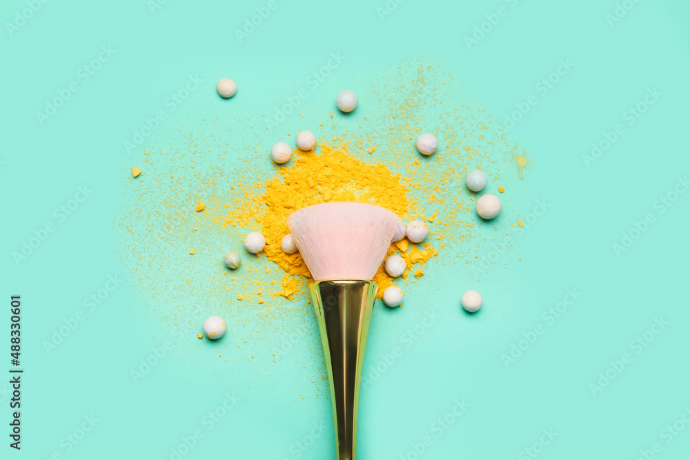 Makeup brush, loose eye shadow and pearl highlighter on color background