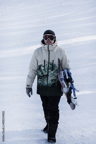 A man with a snowboard in his hand walks along a snow-white mountain slope.