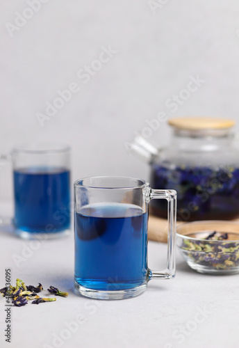 Organic fresh blue anchan tea in a transparent glass cup on a gray table. Herbal Thai tea. Selective focus. Vertical photo.