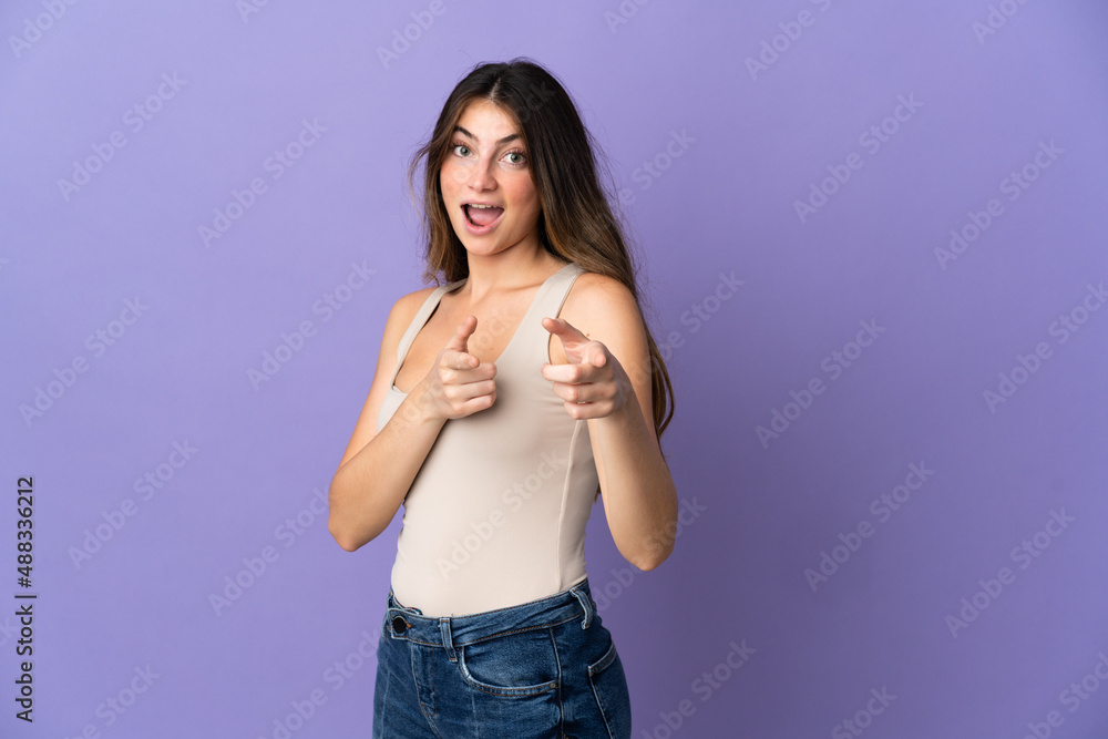 Young caucasian woman isolated on purple background surprised and pointing front Young caucasian woman isolated on purple background surprised and pointing front
