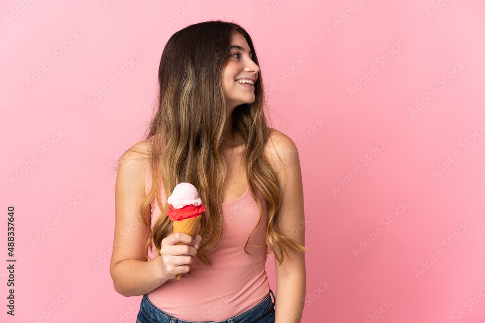 Young caucasian woman with a cornet ice cream isolated on pink background laughing in lateral position Young caucasian woman with a cornet ice cream isolated on pink background laughing in lateral position