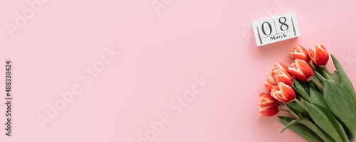 International women's day or eight march banner concept with copy space. 8 march date on perpetual calendar and bunch of red tulip on pink background. Top view or flat lay