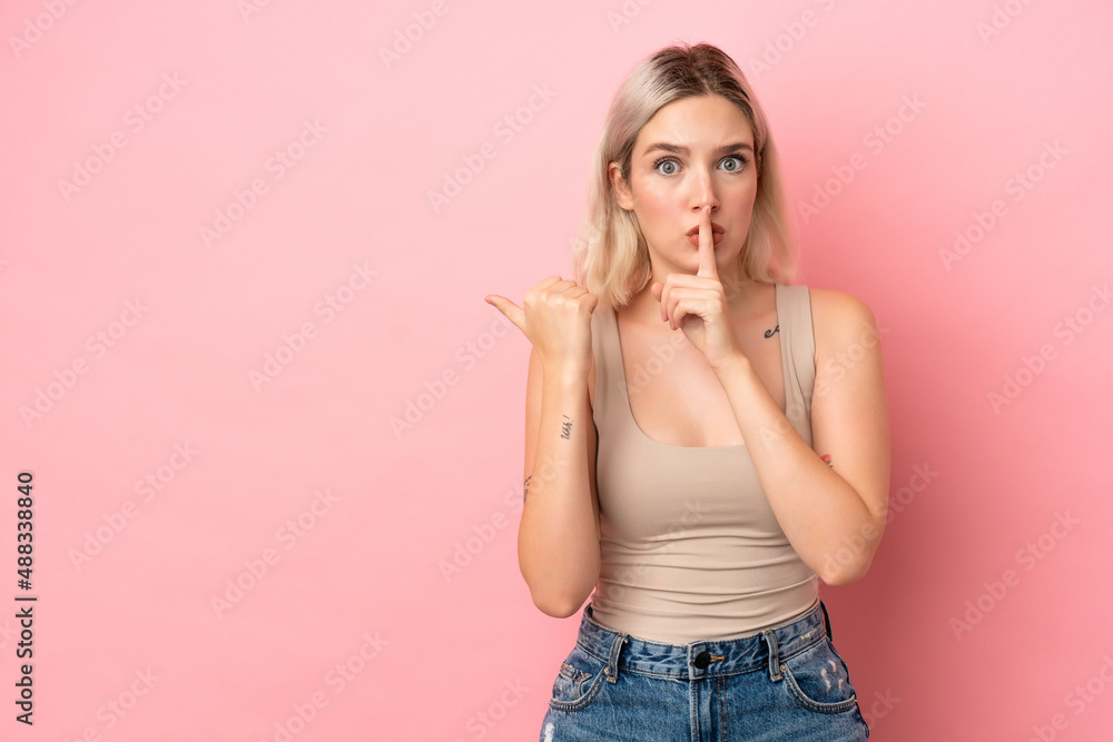 Young caucasian woman isolated on pink background pointing to the side and doing silence gesture Young caucasian woman isolated on pink background pointing to the side and doing silence gesture
