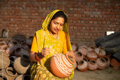 Traditional Indian woman potter artist painting and decorating design on clay pot for sale, handicraft, skill india. photo