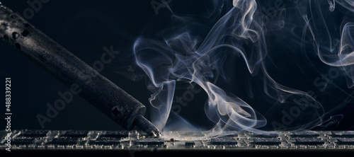 Backdrop of smoking soldering iron on dark background.