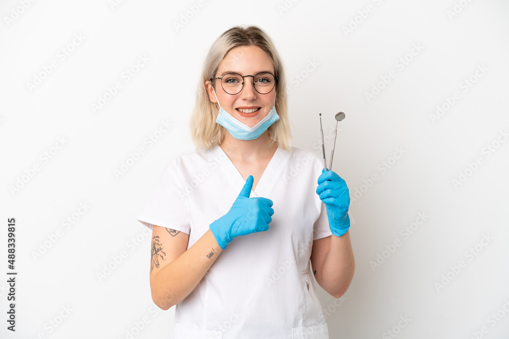 Dentist caucasian woman holding tools isolated on white background giving a thumbs up gesture