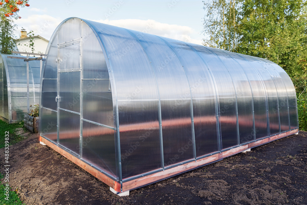 Greenhouse made of polycarbonate on a metal frame. Arched glass glasshouse or greenery for farming natural vegetables in cold climates. Greenhouse made of polycarbonate on a metal frame. Arched glass glasshouse or greenery for farming natural vegetables in cold climates.