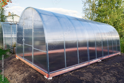 Greenhouse made of polycarbonate on a metal frame. Arched glass glasshouse or greenery for farming natural vegetables in cold climates. © bermuda cat