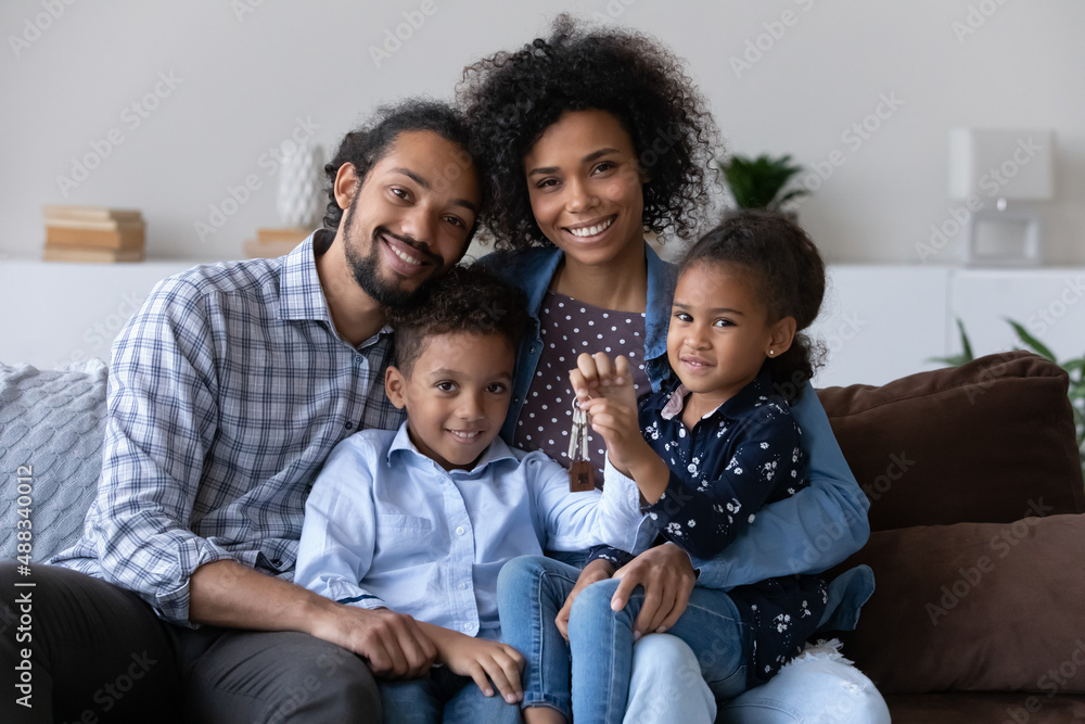 Portrait of happy bonding African American family showing keys to camera, sitting on couch, Joyful adorable small children and caring young multiracial couple parents celebrating moving into own home. Portrait of happy bonding African American family showing keys to camera, sitting on couch, Joyful adorable small children and caring young multiracial couple parents celebrating moving into own home.