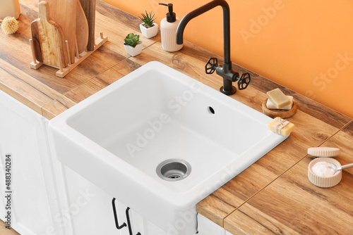 Wooden counter with ceramic sink and cleaning supplies near orange wall