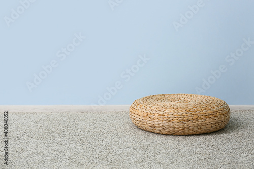Rattan pouf on grey carpet near blue wall