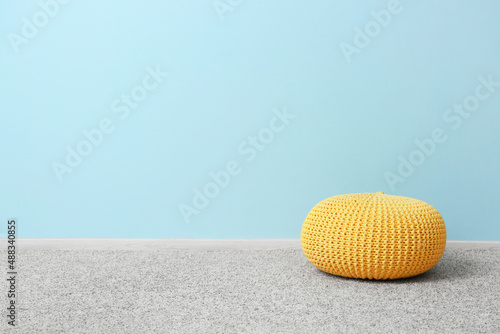 Yellow pouf on grey carpet near blue wall