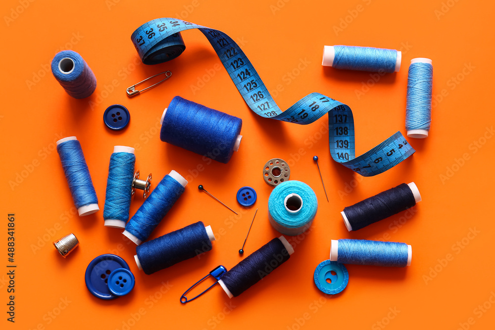 Thread spools with buttons and measuring tape on orange background