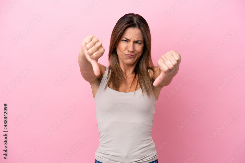 Middle age caucasian woman isolated on pink background showing thumb down with two hands Middle age caucasian woman isolated on pink background showing thumb down with two hands