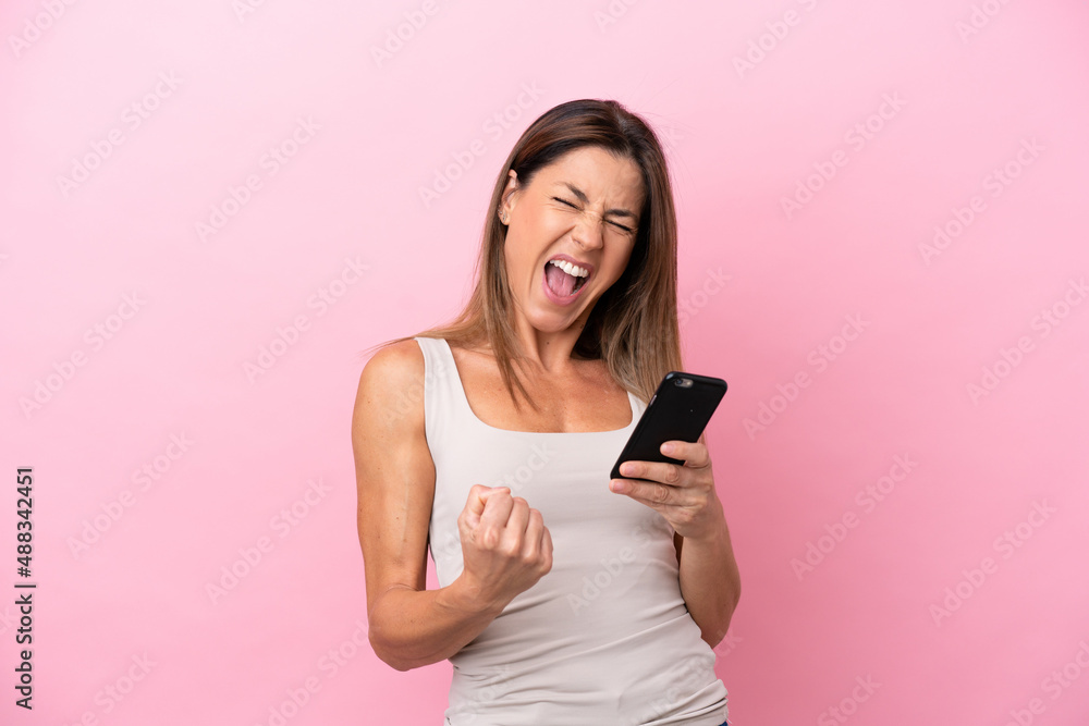 Middle age caucasian woman isolated on pink background with phone in victory position Middle age caucasian woman isolated on pink background with phone in victory position