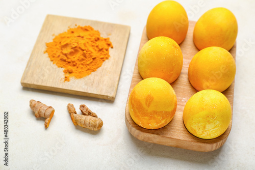 Wooden holder with beautiful Easter eggs and turmeric powder on light background, closeup