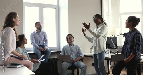 Diverse company staff members brainstorming at briefing in coworking office. Multiracial employees listen to Indian boss tell about project, share knowledge and information. Corporate training concept