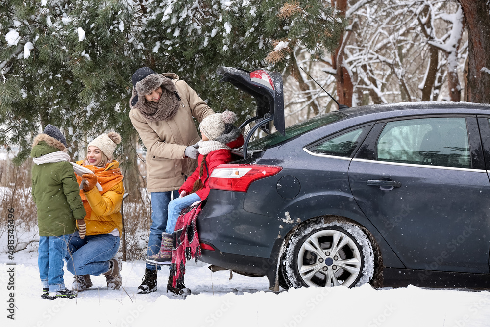 Happy parents and their little children sitting in car trunk on snowy winter day