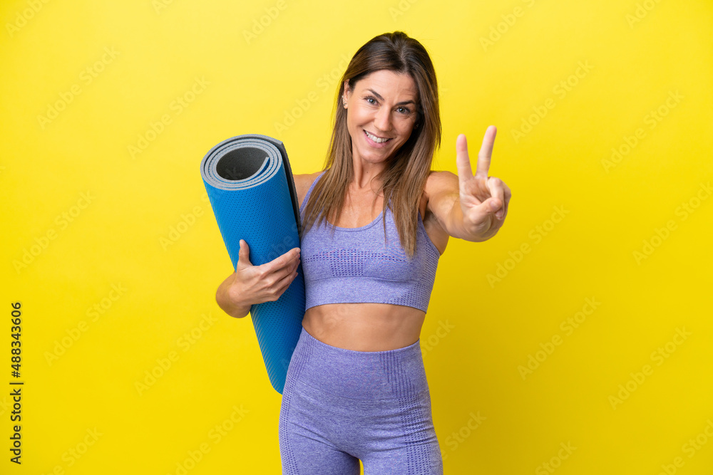 Sport woman going to yoga classes while holding a mat isolated non yellow background smiling and showing victory sign Sport woman going to yoga classes while holding a mat isolated non yellow background smiling and showing victory sign