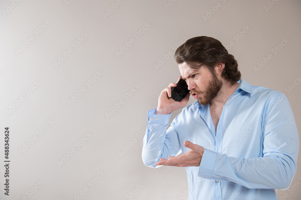 Angry young businessman talking on the phone isolated on light gray background. Angry young businessman talking on the phone isolated on light gray background.