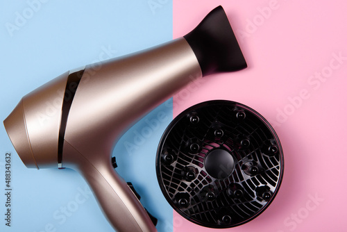 Golden hair dryer on pink and blue paper background, copy space. Top view, flat lay photo