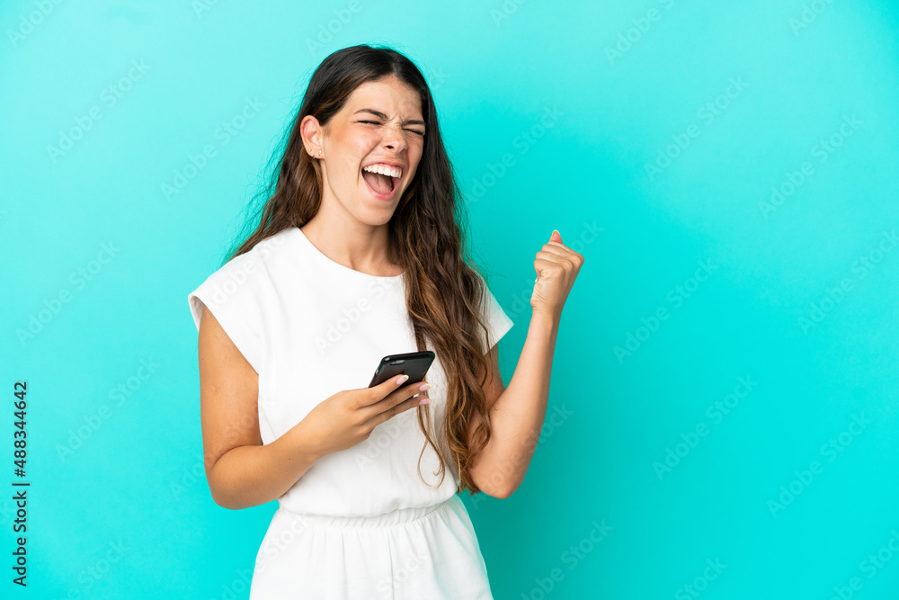 Young caucasian woman isolated on blue background with phone in victory position Young caucasian woman isolated on blue background with phone in victory position
