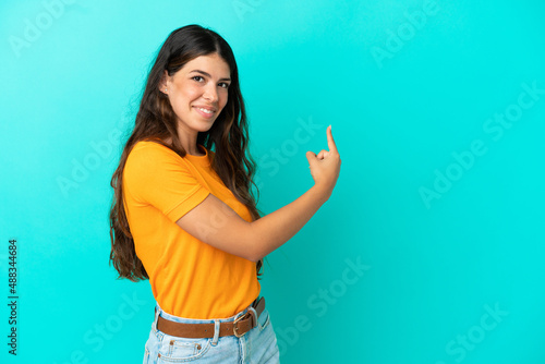 Young caucasian woman isolated on blue background pointing back