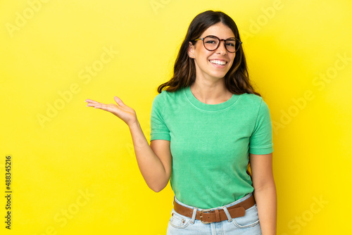 Young caucasian woman isolated on yellow background holding copyspace imaginary on the palm to insert an ad