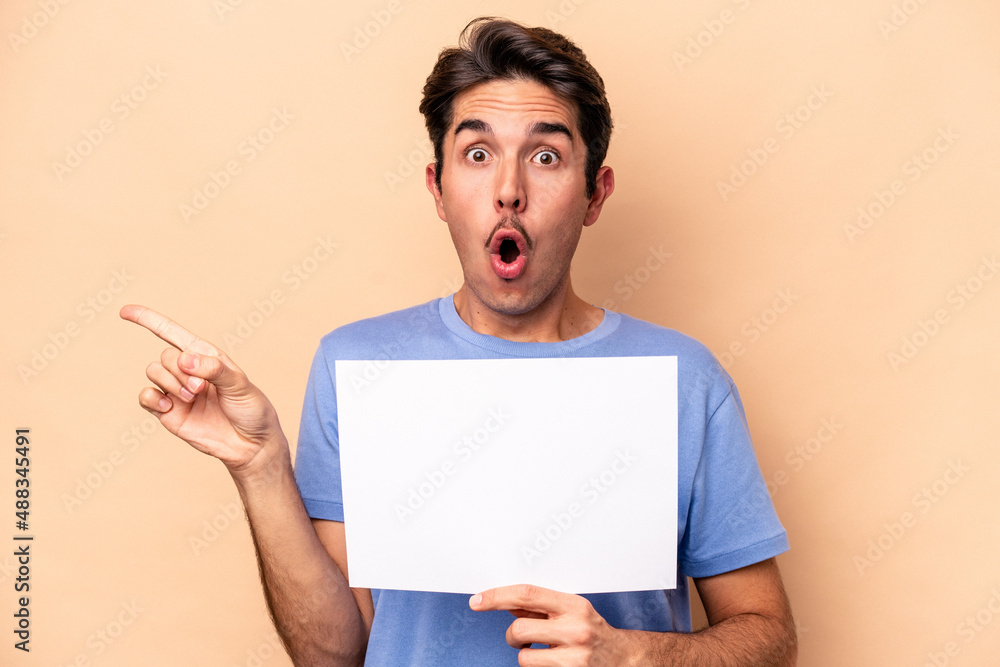 Young caucasian man holding a placard isolated on beige background pointing to the side Young caucasian man holding a placard isolated on beige background pointing to the side
