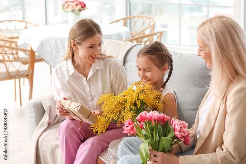 Young woman, her little daughter and mother with flowers at home on International Women's Day