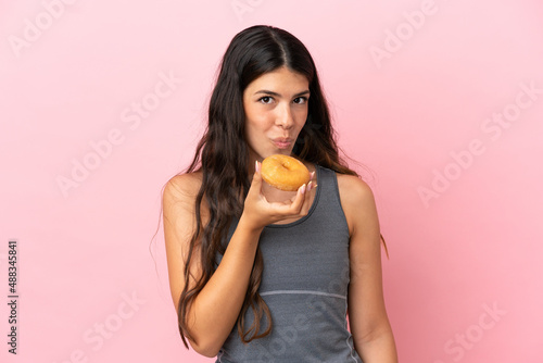 Young caucasian woman isolated on pink background holding a donut
