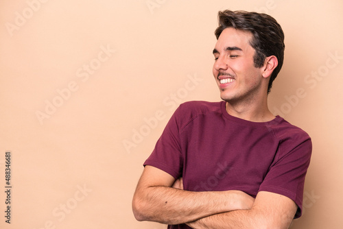 Young caucasian man isolated on beige background smiling confident with crossed arms.