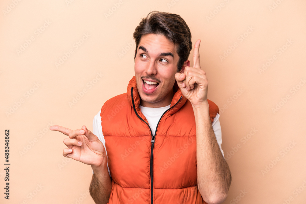 Young caucasian man isolated on beige background pointing to different copy spaces, choosing one of them, showing with finger. Young caucasian man isolated on beige background pointing to different copy spaces, choosing one of them, showing with finger.