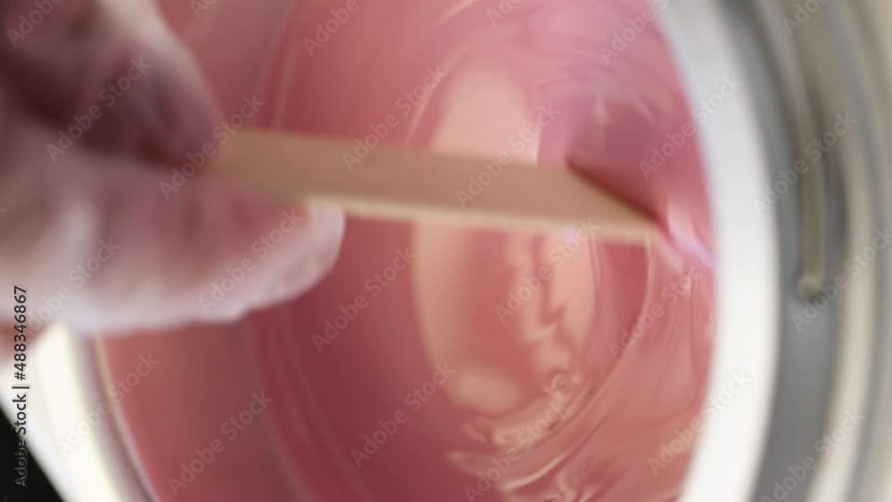 Process of depilatory wax heated and melted in a special device. Beauty master mixes the heating wax with a wooden spatula before the depilation waxing procedure. Vertical video Process of depilatory wax heated and melted in a special device. Beauty master mixes the heating wax with a wooden spatula before the depilation waxing procedure. Vertical video