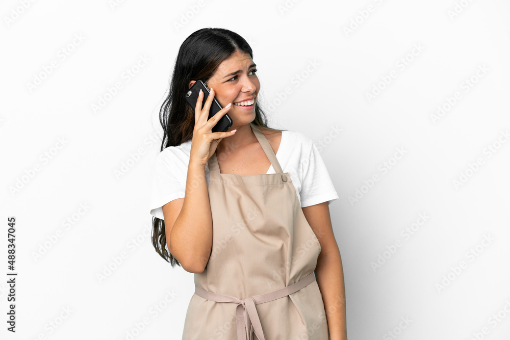 Restaurant waiter over isolated white background keeping a conversation with the mobile phone with someone Restaurant waiter over isolated white background keeping a conversation with the mobile phone with someone