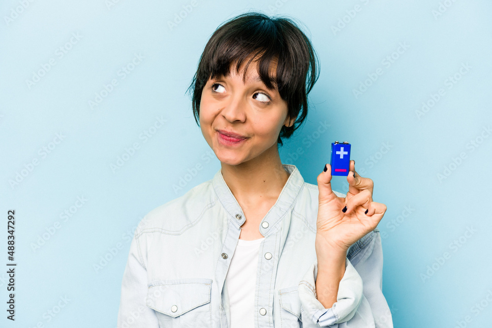Young hispanic woman holding a batterie isolated on blue background dreaming of achieving goals and purposes Young hispanic woman holding a batterie isolated on blue background dreaming of achieving goals and purposes