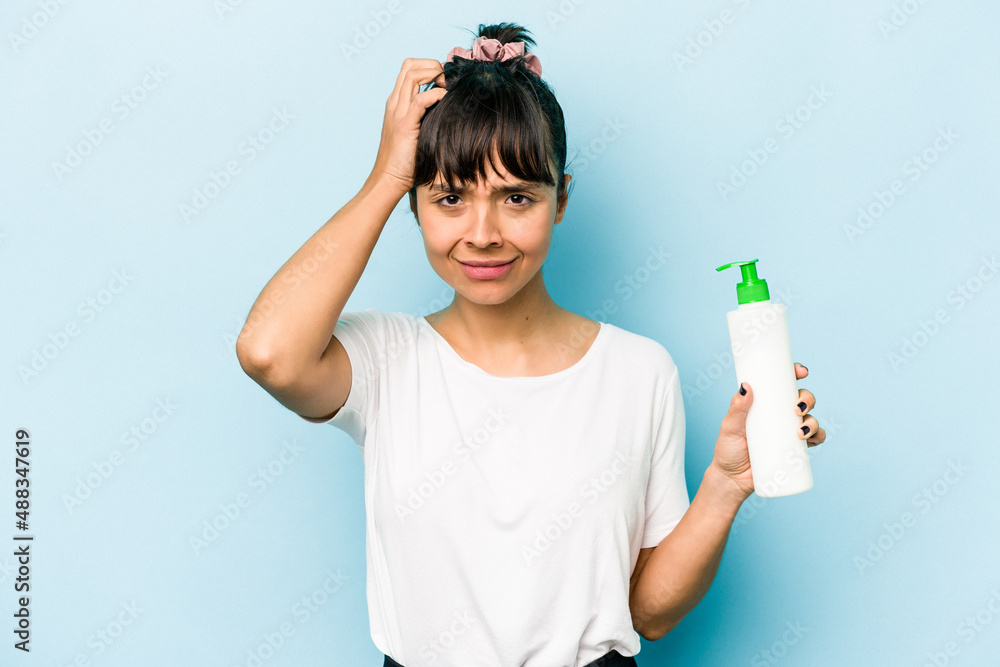 Young hispanic woman holding a body lotion isolated on blue background being shocked, she has remembered important meeting. Young hispanic woman holding a body lotion isolated on blue background being shocked, she has remembered important meeting.