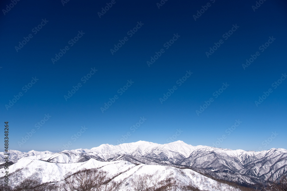 青空の下、新雪の大日ヶ岳山頂から白山を望む