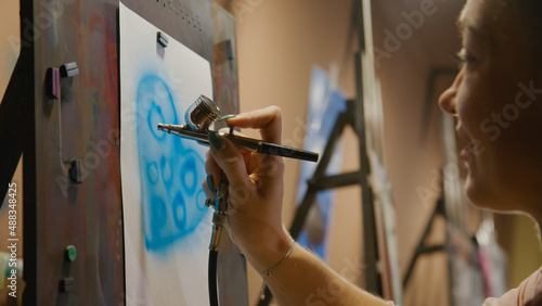 Woman artist learns to paint with airbrush with acrylic dye, paper and easel. Indoors. Concept modern art, airbrushing, aerography, draw spraying picture create sprayer drawing graffiti aerosol spray photo