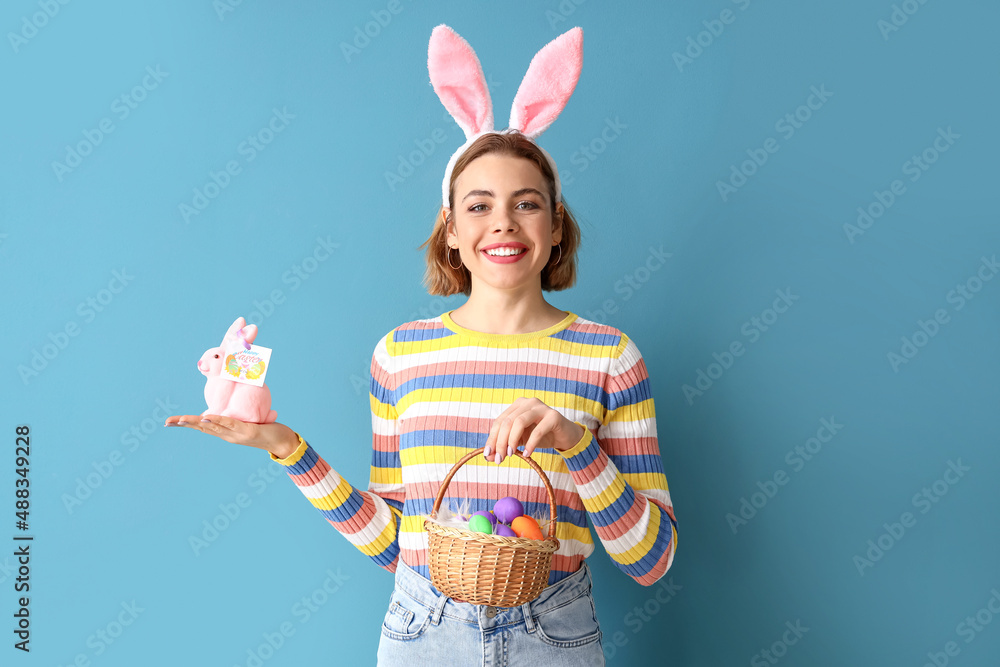 Beautiful young woman with bunny ears, toy rabbit and Easter basket on blue background Beautiful young woman with bunny ears, toy rabbit and Easter basket on blue background