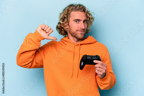Young caucasian man playing with a video game controller isolated on blue background feels proud and self confident, example to follow.
