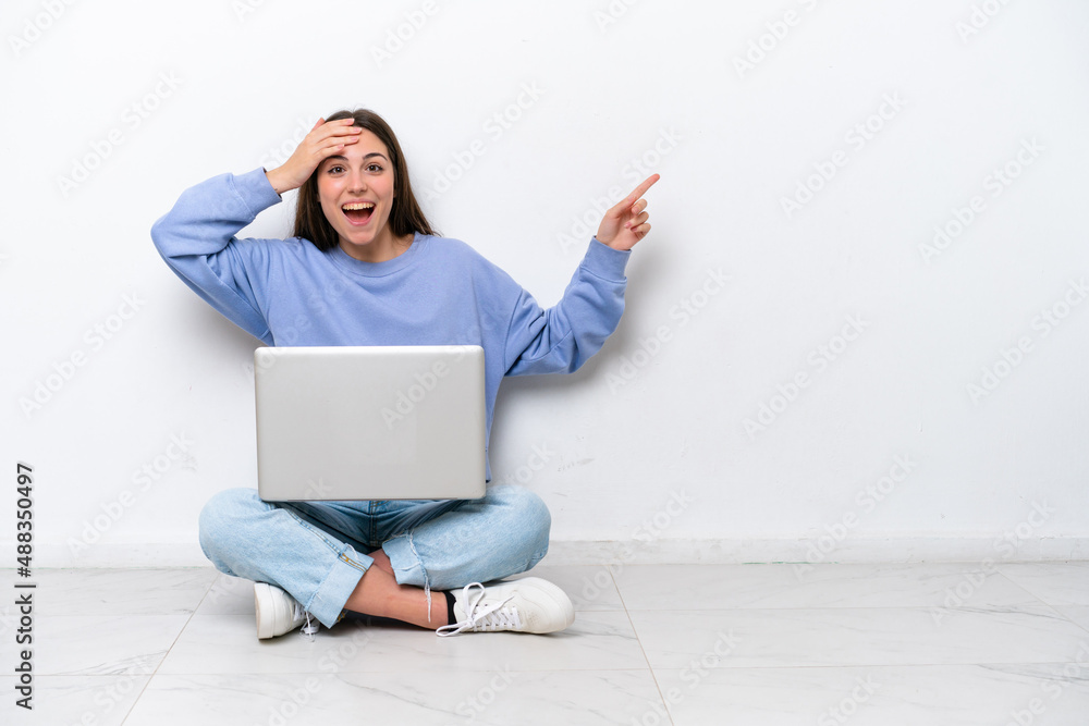 Young caucasian woman with laptop sitting on the floor isolated on white background surprised and pointing finger to the side Young caucasian woman with laptop sitting on the floor isolated on white background surprised and pointing finger to the side