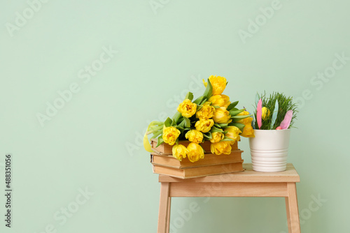 Bouquet of tulips, stack of books and Easter decor on stepladder stool near color wall © Pixel-Shot