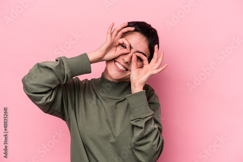 Young caucasian woman isolated on pink background showing okay sign over eyes