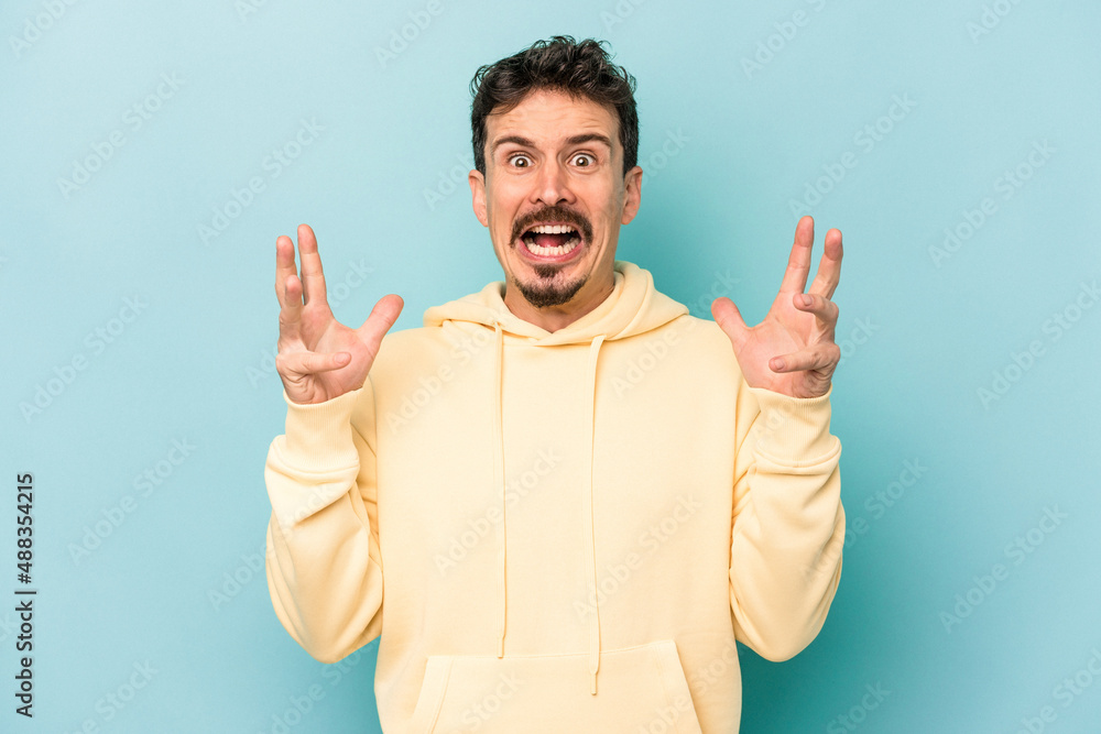 Young caucasian man isolated on blue background screaming to the sky, looking up, frustrated. Young caucasian man isolated on blue background screaming to the sky, looking up, frustrated.