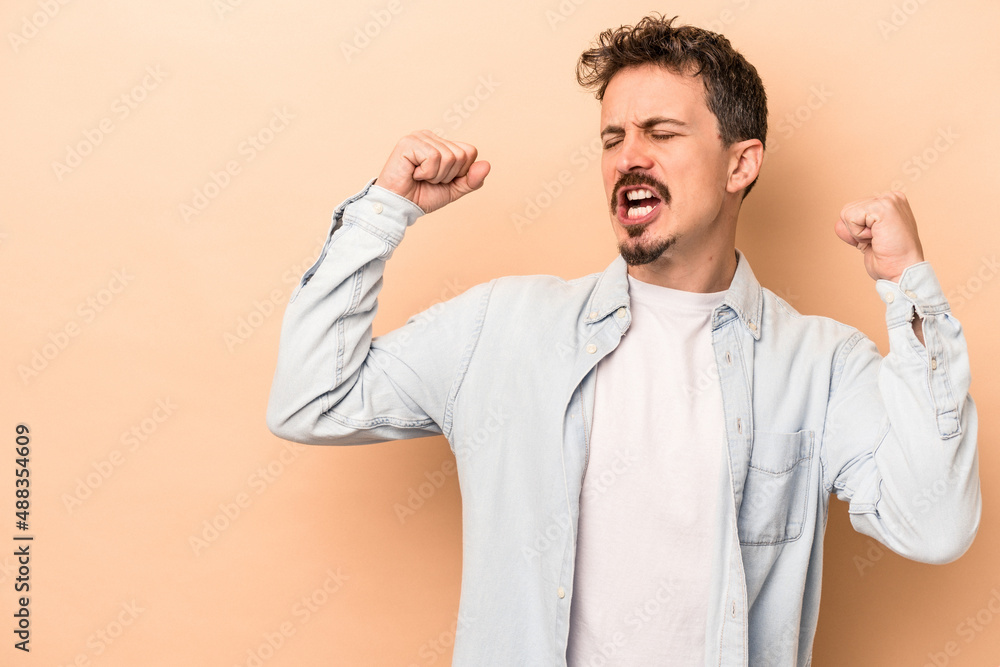 Young caucasian man isolated on beige background raising fist after a victory, winner concept. Young caucasian man isolated on beige background raising fist after a victory, winner concept.